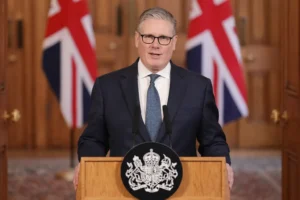 UK Prime Minister Keir Starmer delivering a statement from a podium with Union Jack flags in the background regarding the use of UK bases amid Iran tensions.